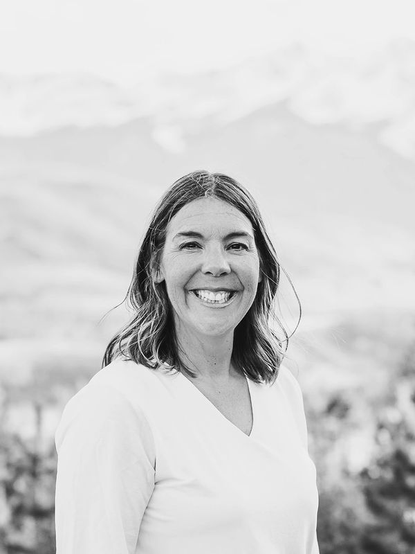 Smiling woman in white top outdoors with mountains in the background.