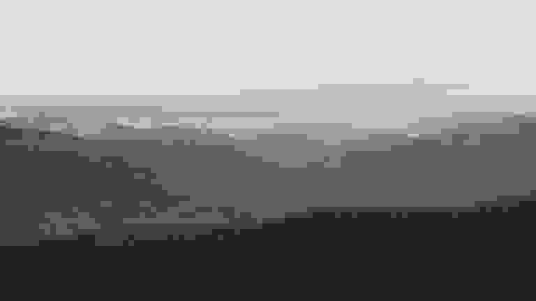 Mountain range at dusk with pink-tinged clouds and forested hills.