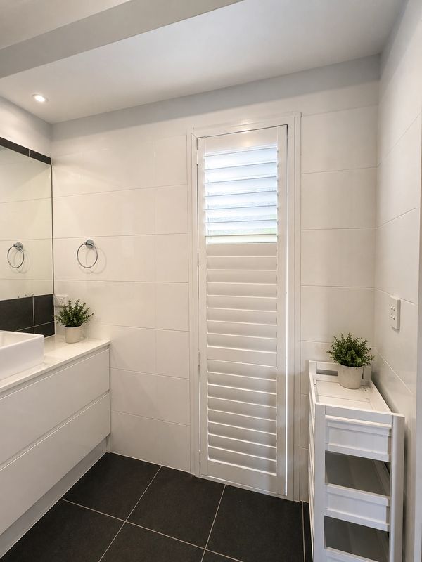 Minimalist white bathroom with black floor tiles and green potted plants.