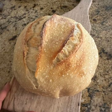 Freshly baked round artisan bread with a crisp crust on a wooden paddle.