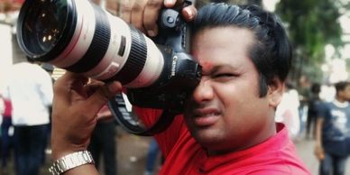 Man in red shirt taking a photo with a professional camera outdoors.