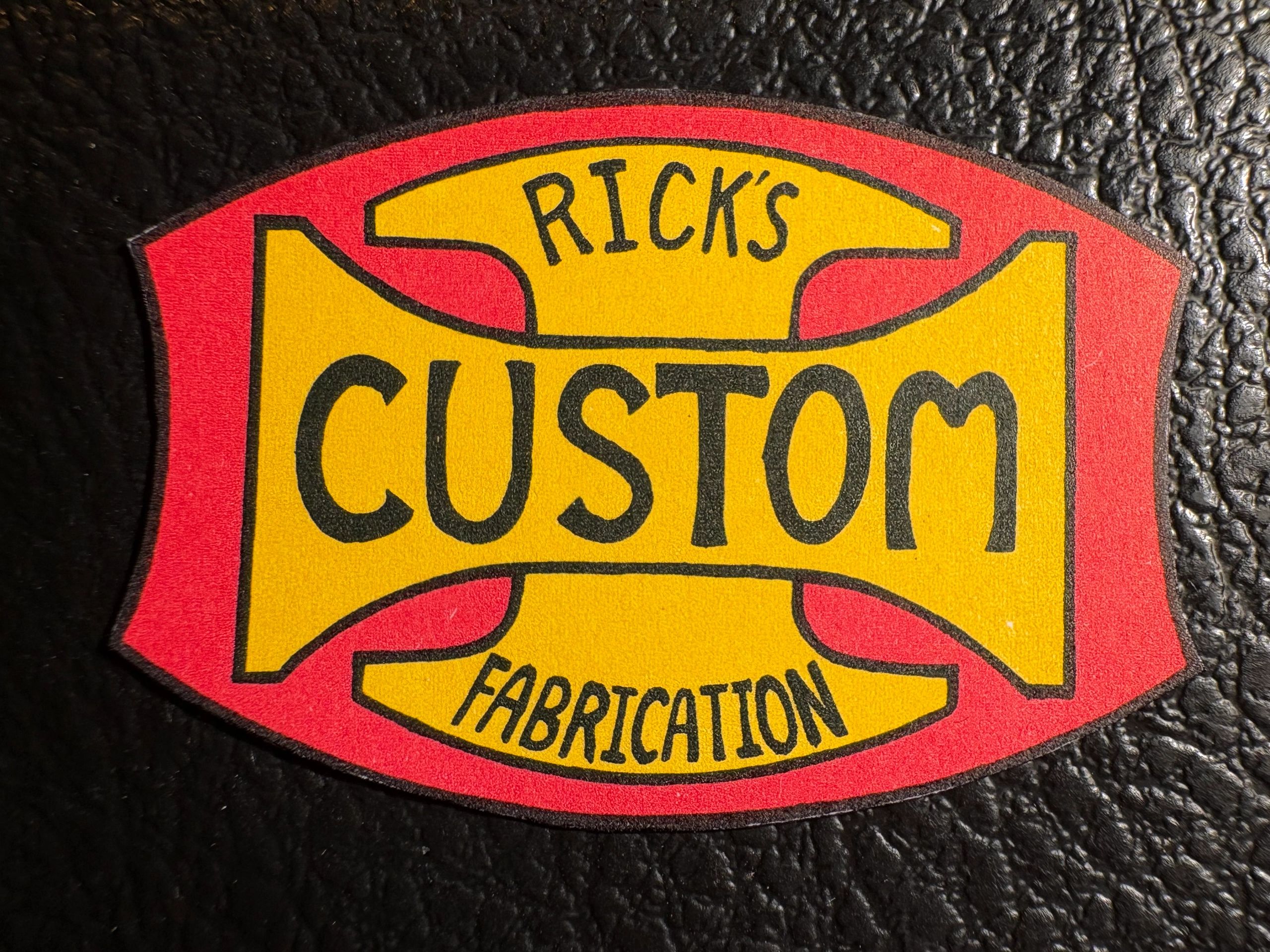 A colorful patch reading "Rick's Custom Fabrication" on a textured black background.