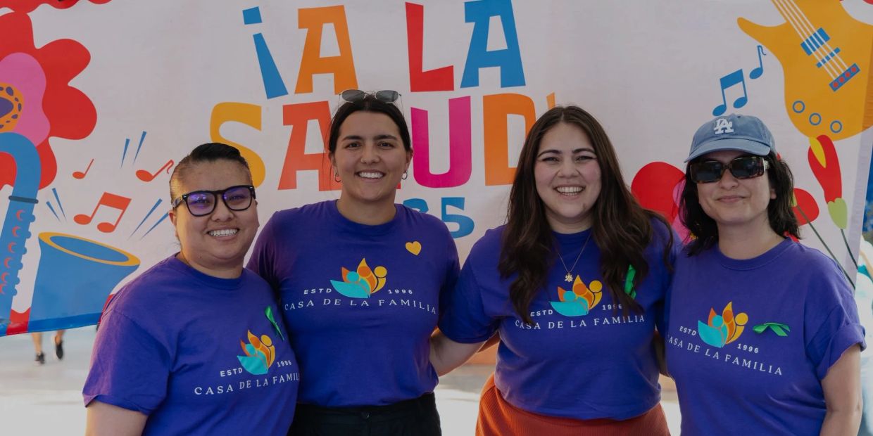 Cuatro mujeres sonrientes con camisetas de "Casa de la Familia" en evento saludable.