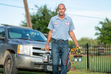 Technician carrying HVAC gauges and tools near a truck.
