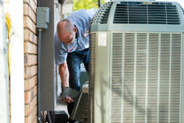Technician inspecting an air conditioning unit outdoors.