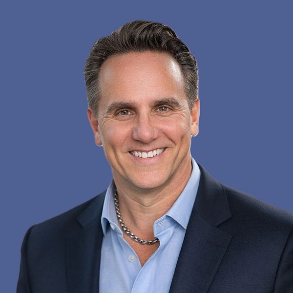 Smiling man in a blue suit and light blue shirt with a silver chain necklace.