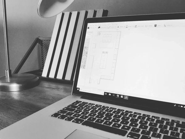 Black and white photo of a laptop displaying a design on a wooden desk.