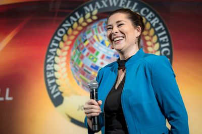 Photo of female holding microphone, smiling, and wearing a blue jacket with a black top 