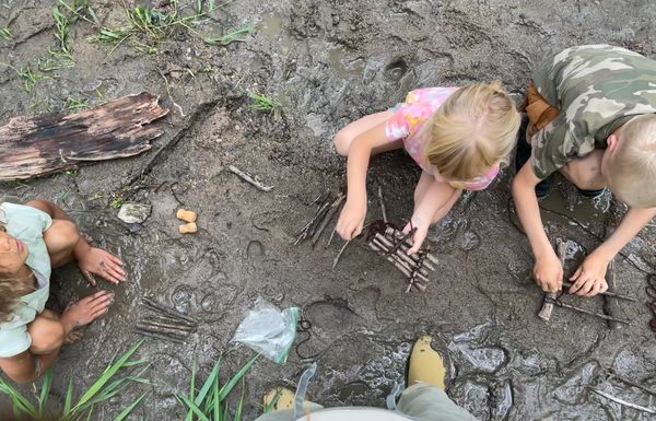 Kids playing with sticks in the mud outdoors.