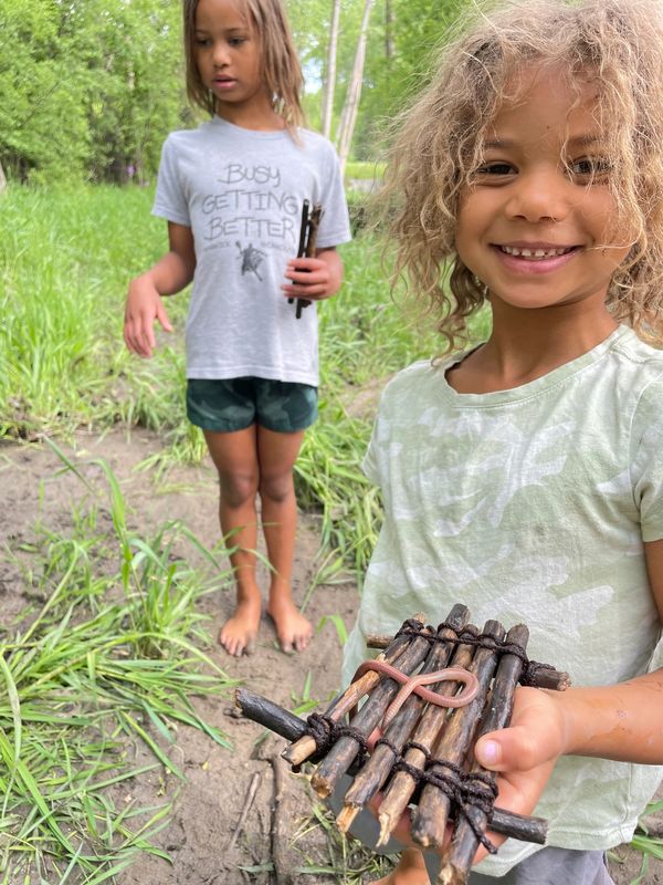Smiling child holding a handmade raft with another child in the background.