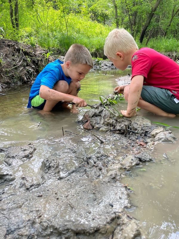 Two boys playing in a muddy creek.