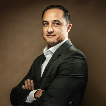 Confident man in a suit with arms crossed against a brown background.
