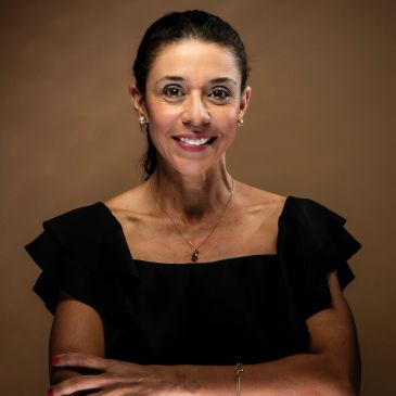 Confident woman in a black dress smiling against a brown background.