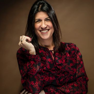 Smiling woman with dark hair wearing a red and black floral blouse.