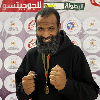 A bearded man with a medal poses confidently with fists up at a championship event.