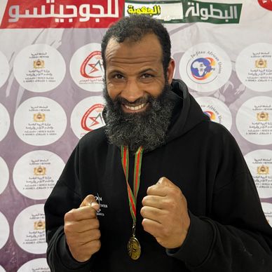 A bearded man with a medal poses confidently with fists up at a championship event.