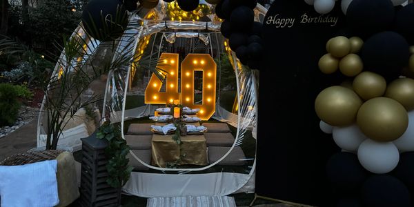 Elegant outdoor 40th birthday setup with illuminated numbers and black, gold, and white balloons.