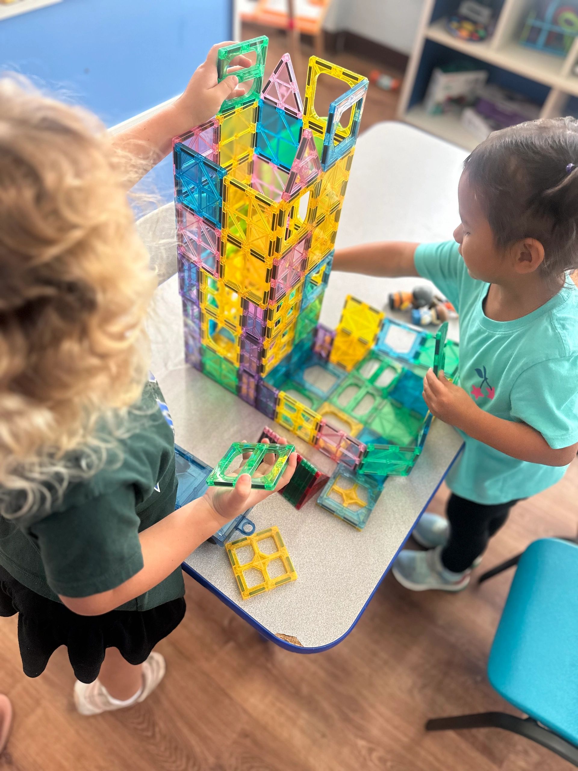 Two kids building a colorful tower with magnetic tiles.
