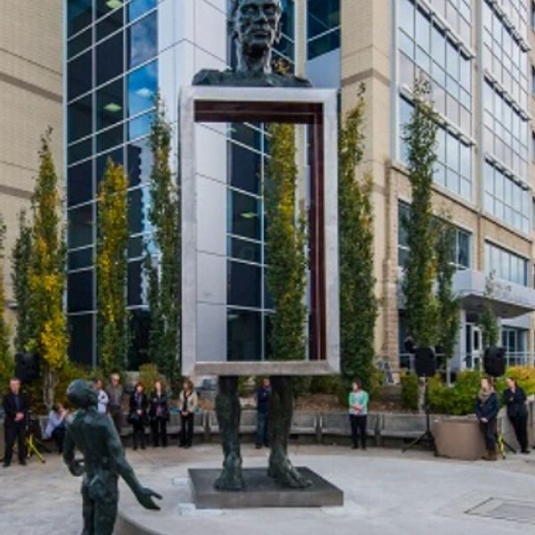 Sculpture with a hollow rectangular frame and a bust on top, surrounded by people in an urban plaza.
