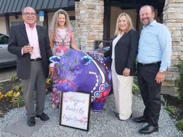 Four people posing with a colorful painted cow sculpture outdoors.