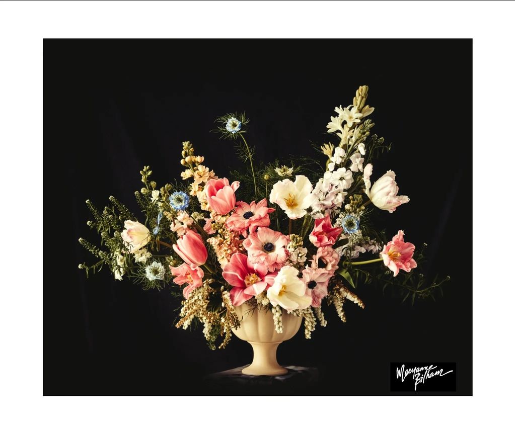 Elegant bouquet of mixed flowers in a cream vase against black background.