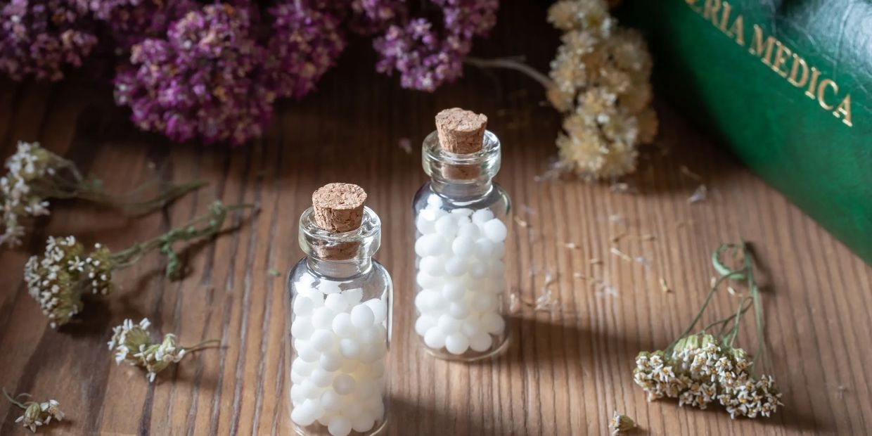Two small corked vials filled with homeopathic remedies on a table of dried flowers. Homeopathy for hay fever