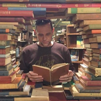 Man reading a book framed by stacks of books.