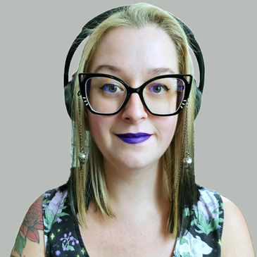 Yelka looking at camera with over-ear headphones, purple lipstick with black and silver hair