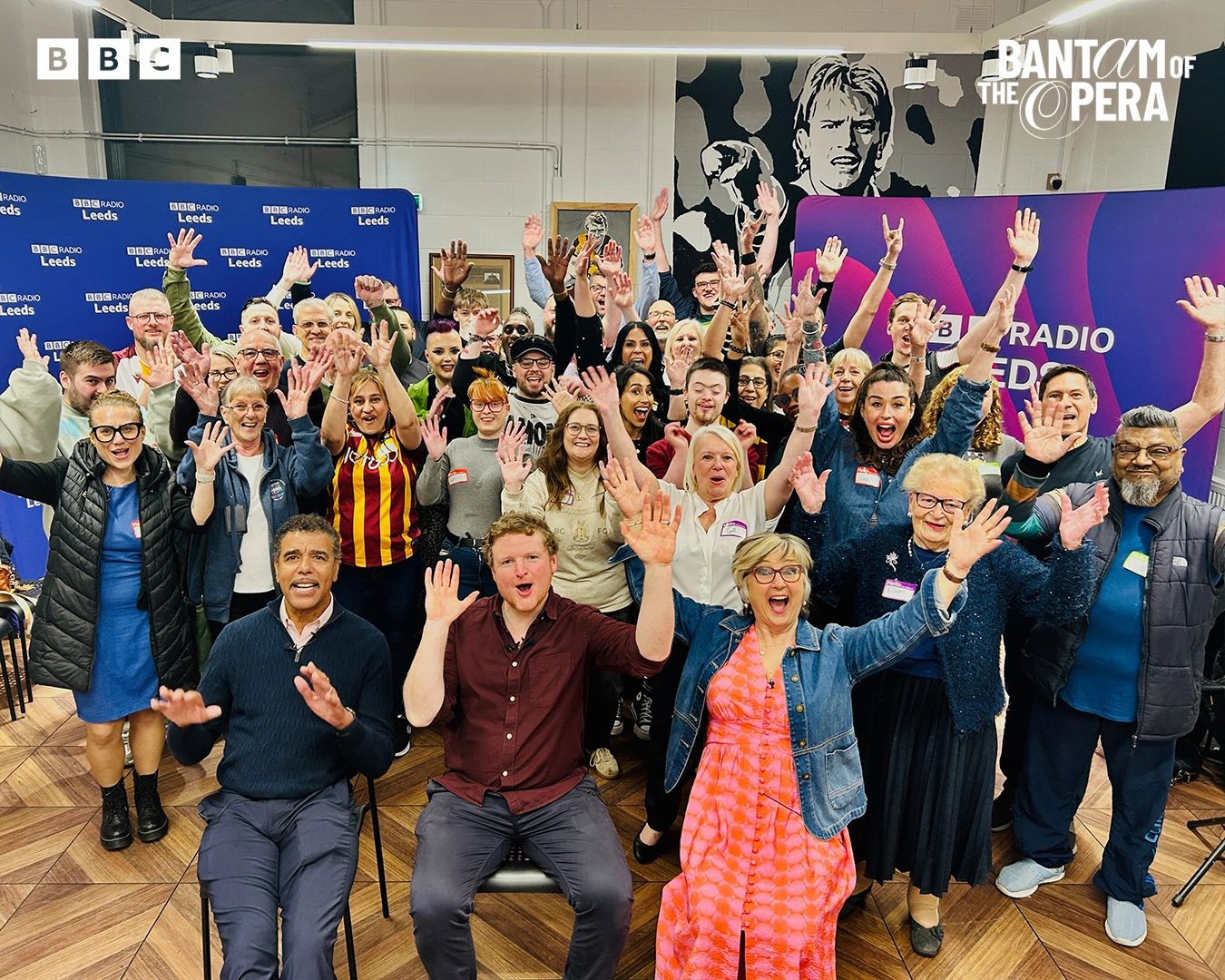 A large group of diverse people smiling and waving at a BBC Radio Leeds event.
