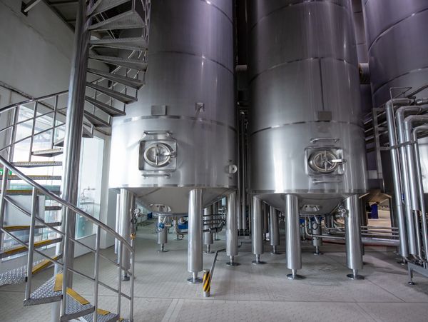 Large stainless steel industrial tanks in a clean facility with a spiral staircase.