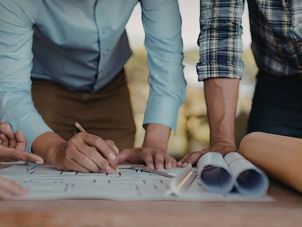 Two people collaborating on architectural plans at a wooden table.