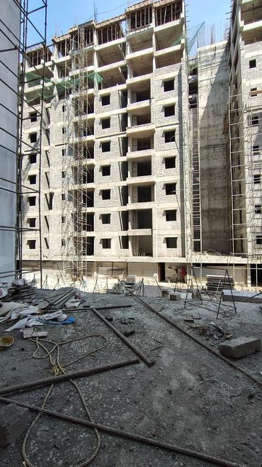 High-rise building under construction with scaffolding and construction materials scattered.