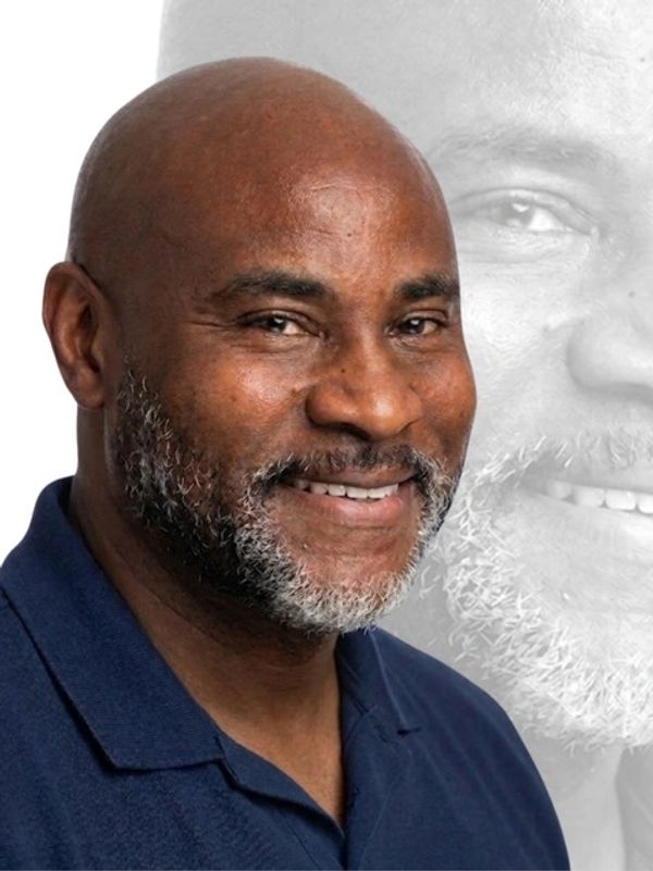 Smiling bald man with salt-and-pepper beard in navy blue shirt.