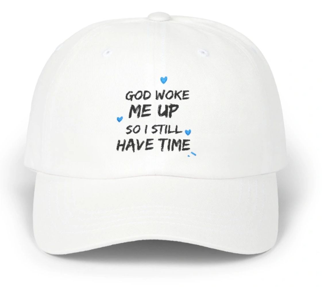 White cap with the motivational phrase 'God woke me up so I still have time' embroidered on it.