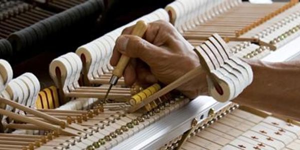 A person tuning the internal strings of a piano with a tuning tool.