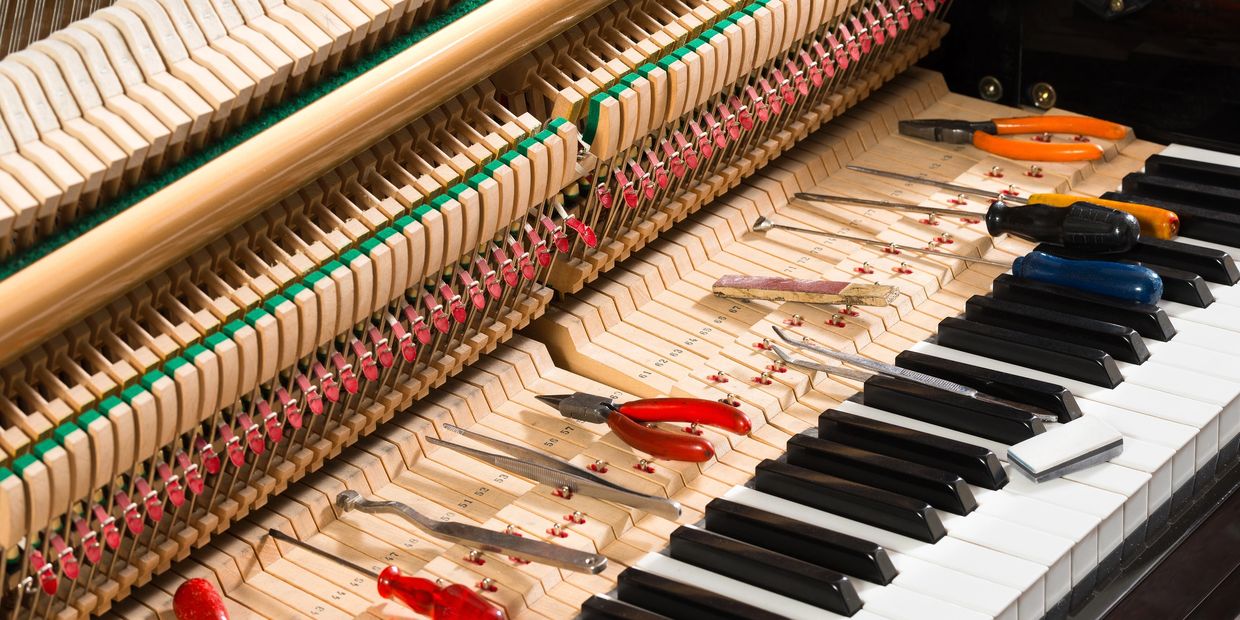 Open piano with tools laid out for tuning and repair.