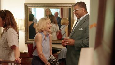 Two people smiling and conversing in a warmly lit room with a mirror reflecting others.