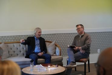Two men engaged in a discussion in a cozy room setting.