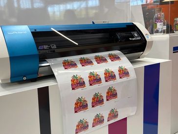 Roland printer producing colorful Amsterdam stickers on glossy paper.