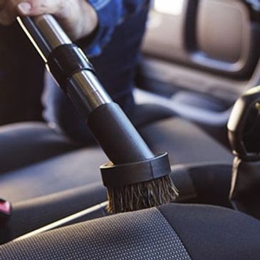 Man with a shampoo brush about to scrub inside a car with cloth upholstery.