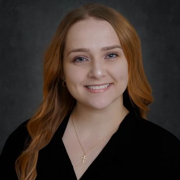 Young woman with red hair smiling against a dark background.