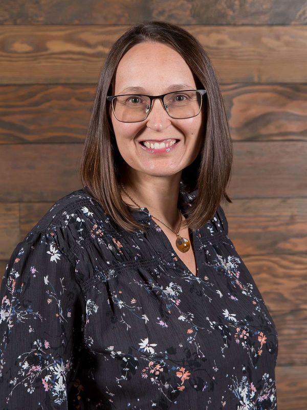 Woman smiling standing in front of a wooden background.