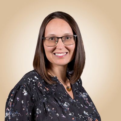 Smiling woman with glasses wearing a floral blouse against a beige background.