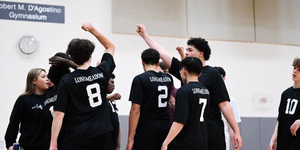 High school volleyball team in black jerseys celebrating a play in the gymnasium.