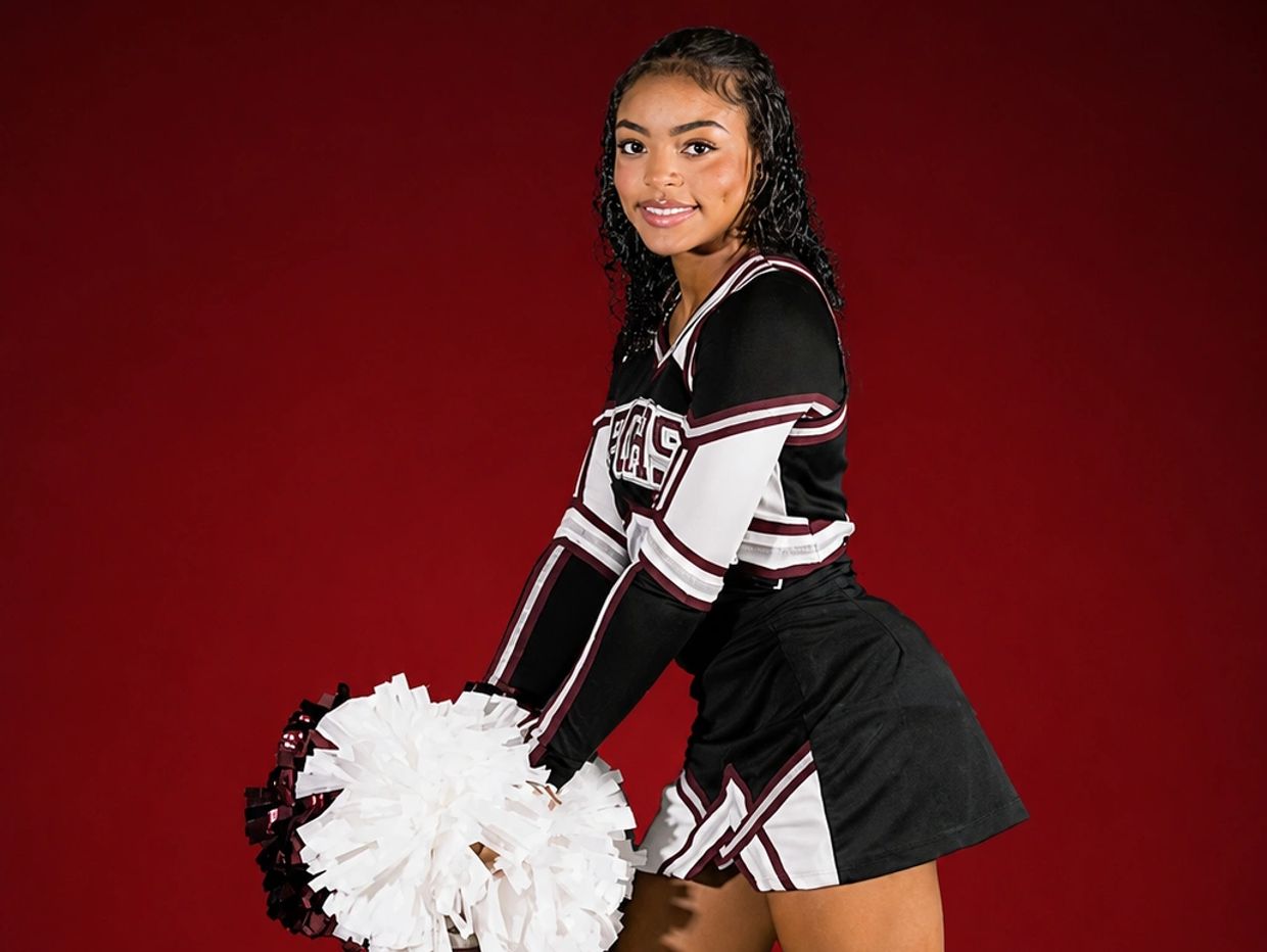 Cheerleader posing in uniform with pom-poms.