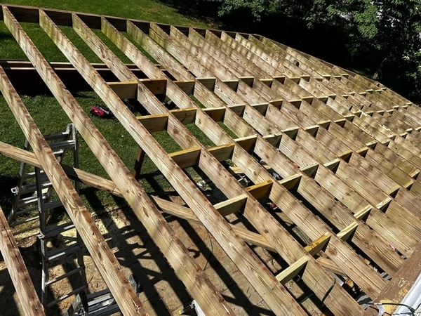 Wooden frame structure of a deck under construction on a sunny day.