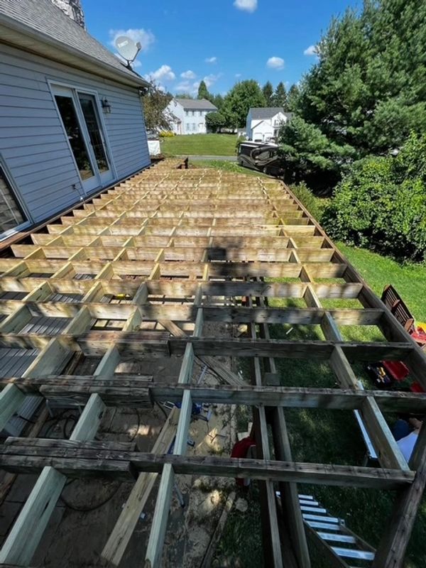 Wooden deck frame under construction beside a house on a sunny day.