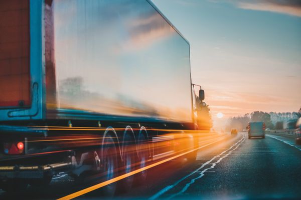 Semi-Truck driving down highway into sunset.
