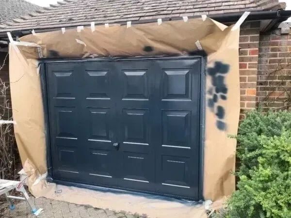 Freshly painted black garage door with protective masking around the brickwork for a neat  finish.