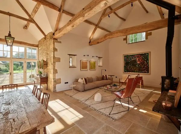 Spacious country-style living room with exposed wooden beams, stone walls, neutral painted walls.